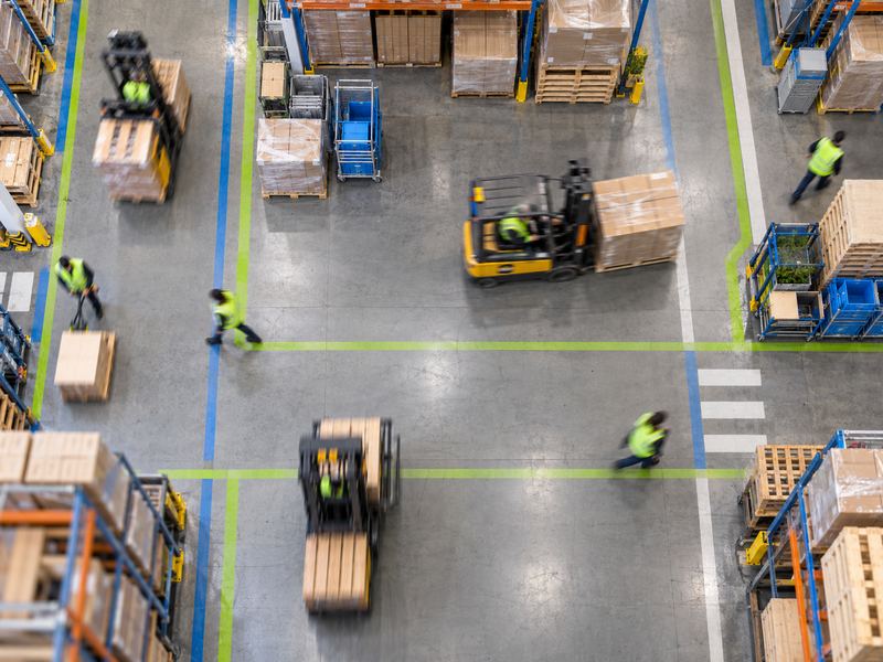 Forklifts and workers moving through a warehouse from above